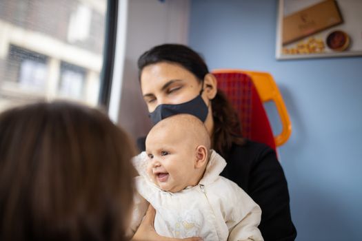 Woman with closed eyes sitting next to a window in a bus, holding her smiling baby who looks happily through the window