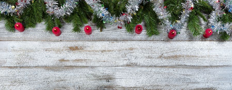 Border of Evergreen branches with tinsel and burning red candle decorations for Christmas or New Year holiday background 