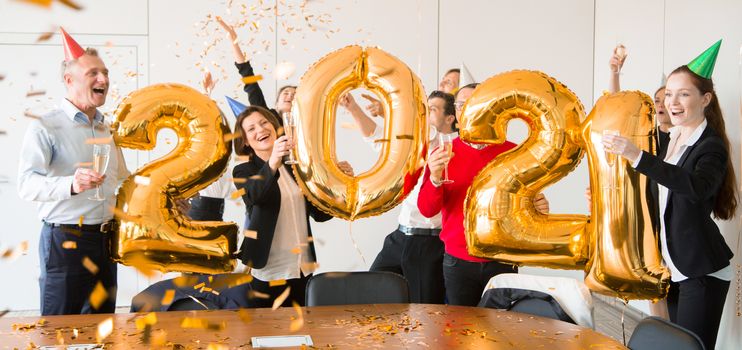 Business people are celebrating holiday in modern office drinking champagne and having fun in coworking. Merry Christmas and Happy New Year 2021. Balloon numbers