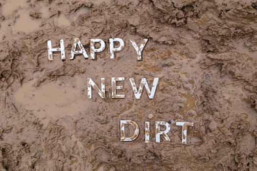 the words happy new dirt laid with silver metal letters on wet mud surface in directly above perspective under cloudy autumn day light