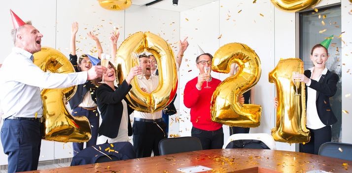 Business people are celebrating holiday in modern office drinking champagne and having fun in coworking. Merry Christmas and Happy New Year 2021. Balloon numbers