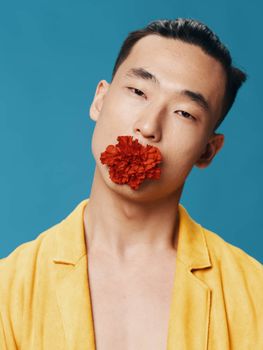 Asian man with red flower in teeth yellow coat bared torso close-up cropped view. High quality photo
