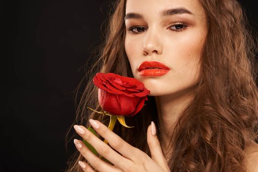 woman with a red rose on a dark background long hair makeup red lips. High quality photo