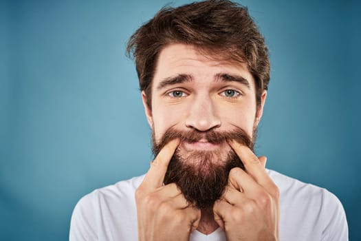 Bearded man displeased facial expression emotions close-up blue background white t-shirt. High quality photo