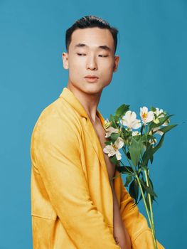 guy in yellow coat asian appearance bouquet of white flowers and blue background side view. High quality photo