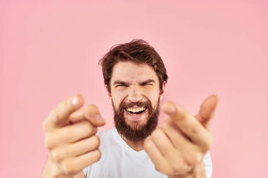 Bearded man in white t-shirt gesturing with hands facial expression close up pink background. High quality photo