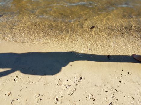 shadow of person on shore of beach with sand and water