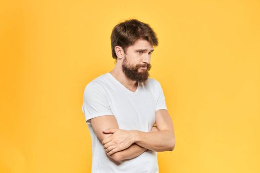 Bearded man in a white T-shirt gestures with his hands emotions studio yellow background. High quality photo