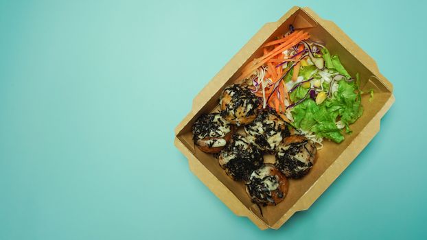Japanese food Takoyaki with vegetables salad in paper box.