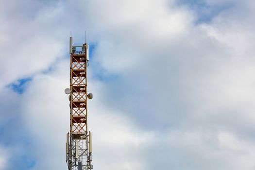 Telecommunication tower of 3G, 4G and 5G cellular communication with antennas against a blue cloudy sky.