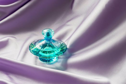 Perfume bottle on lilac silk folded fabric background. Luxery Scent fragrance cosmetic beauty product.