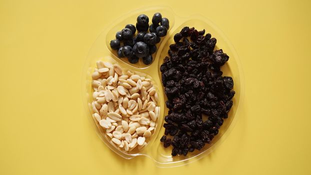 Berries ad nuts in round plastic container for food storage - yellow background