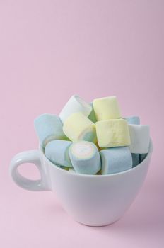 Colorful marshmallows in white cup on pink background.