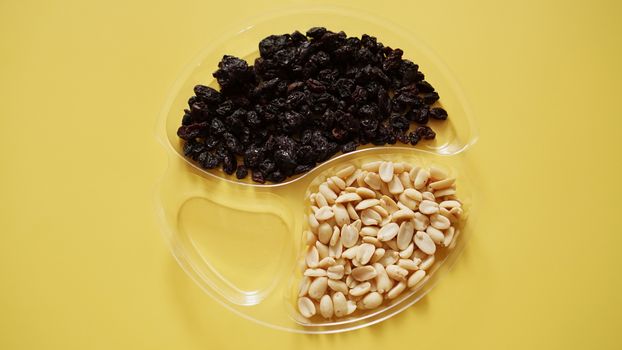 Dry fruits and nuts in round plastic container for food storage - yellow background. One container is empty
