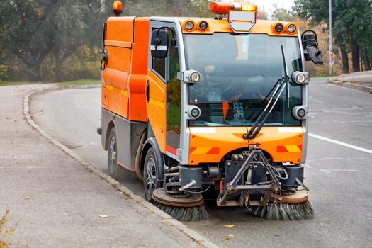 A small street sweeper with two independently controllable, hydraulically adjustable front brushes cleans the road in a residential area of the city.