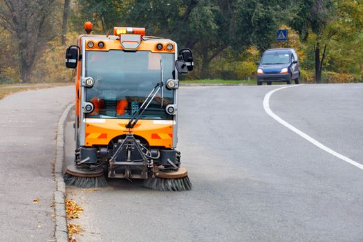 A small street sweeper with two hydraulically adjustable front brushes cleans the road in a residential area of the city, copy space.