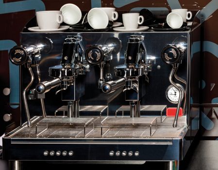 A metal professional coffee maker and white coffee cups on it. Low key.