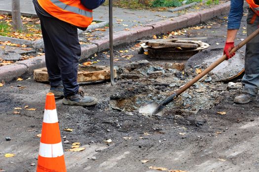 Road workers, dressed in reflective clothing, use a crowbar and a shovel to dismantle an old sewer manhole, copy space.