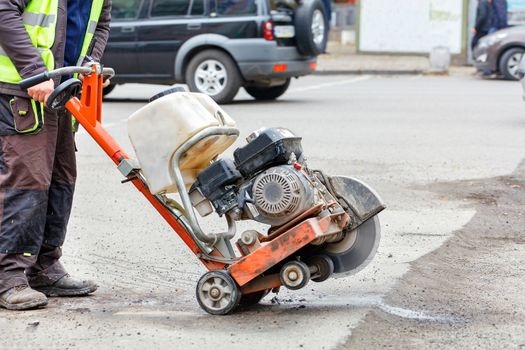 A road worker in reflective clothing moves a petrol cutter with a working diamond saw blade to cut through the bad old asphalt on the road. Copy space.