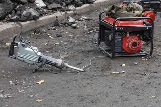 Electric jackhammer with a gasoline generator ready to work against the background of a workplace with a road section being repaired, copy space.
