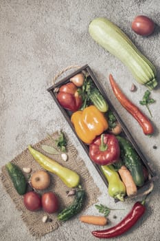 In a wooden container and on a napkin a variety of ripe vegetables: tomatoes, peppers, cucumbers, parsley, zucchini. Top view with copy space. Flat lay