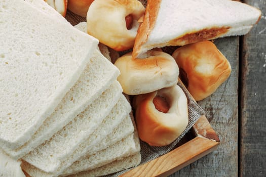 Many breads on wooden tray of table.