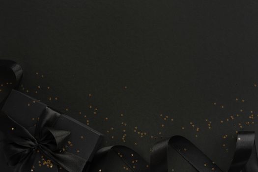 Black friday gift, paper box with silk ribbon bow and golden glitter stars on black paper background with copy space for text, flat lay top view template