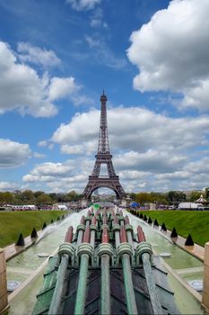 The Eiffel Tower in Paris from the side of Trocadero Square and the Trocadero Fountain on a background of blue sky and clouds.
