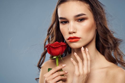 Woman portrait with red rose near the face on gray background and makeup curly hair. High quality photo