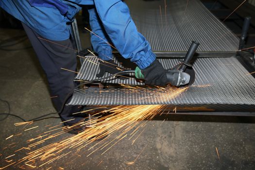 A worker cuts an iron mesh netting with an iron circle in a locksmith's workshop. Sparks fly