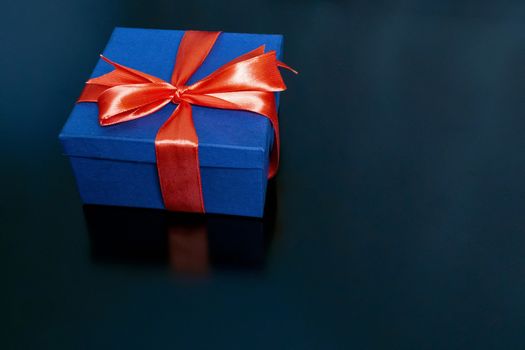 on a black background is a dark blue gift box tied with a red ribbon