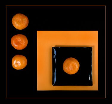 Composition of orange mandarin and black square plate on an orange table. Flat lay. View from above.
