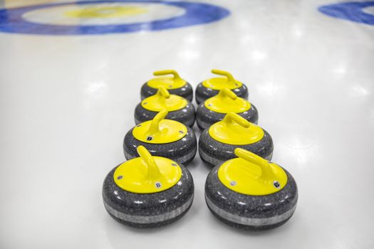 The curling stone or rock is made of granite with yellow handles lie on the ice, in the background a circular target marked on the ice home