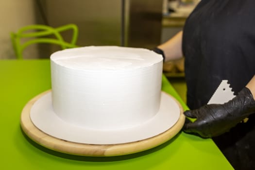 Cake cooking. The chef cook makes the mold for the preparation of a white round cake. Daub with white cream and smooths with a spatula.