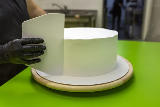 Cake cooking. The chef cook makes the mold for the preparation of a white round cake. Daub with white cream and smooths with a spatula.