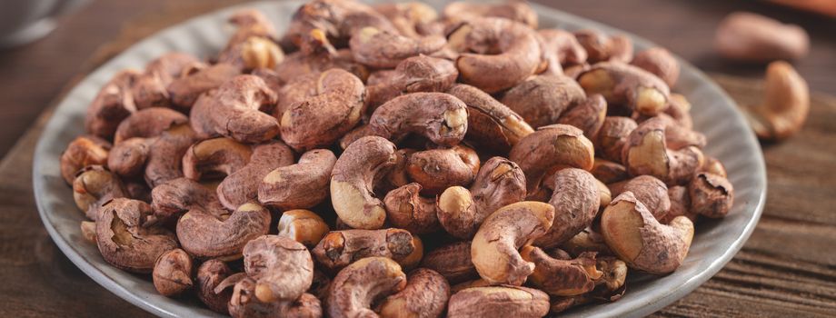Cashew nuts with peel in a plate on wooden tray and table background, healthy raw food concept.