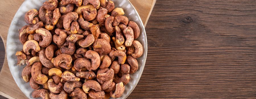 Cashew nuts with peel in a plate on wooden tray and table background, healthy raw food concept.