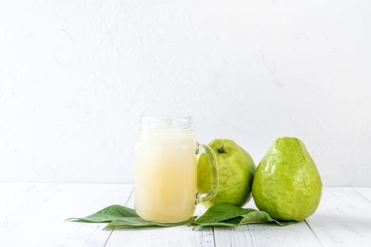 Delicious beautiful guava fruit with fresh juice set isolated on bright white wooden table background, close up.