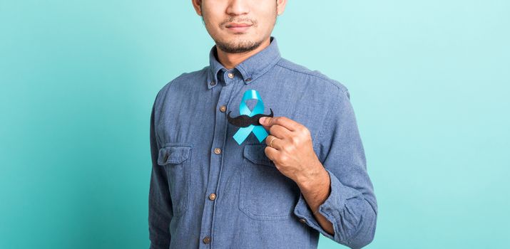 Asian portrait happy handsome man posing he holding a light blue ribbon and mustache, studio shot isolated on blue background, Prostate Cancer Awareness in November concept