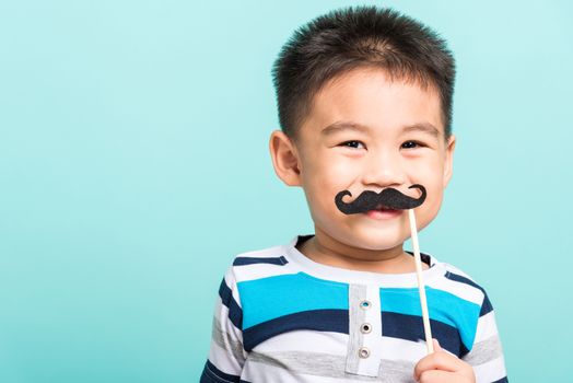 Funny happy hipster kid holding black mustache props for the photo booth close face, studio shot isolated on a blue background, Men health awareness, Prostate Cancer Awareness