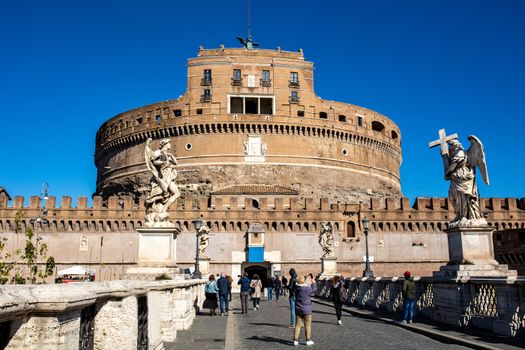 Frontal view of the Castel Sant'Angelo against the blue sky in Rome, Italy. tourists walk on the bridge