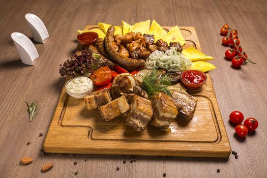 grill set on a wooden board grilled chicken, pork skewers, pork ribs, grilled sausages, vegetables, marinated onions, pita bread, barbecue, tar-tar sauce, ketchup