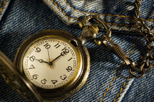 Vintage pocket watch is placed over an old blue denim shirt and the morning sun shines down in the top right corner. The concept of time importance. Closeup and copy space for text or your article.