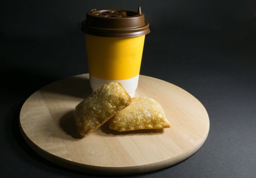 Glass of coffee and fried pie on a wooden stand on black background