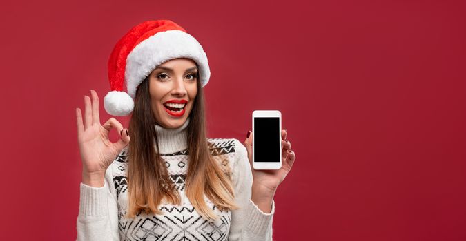 Close up portrait beautifiul caucasian woman in red Santa hat on red studio background. Christmas New Year holiday concept. Cute girl teeth smiling positive emotions with free copy space