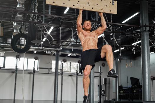 Man climbing pegboard gym athlete training arm strength stamina alpinism indoor. Athlete caucasian guy hanging from his hands wooden campus board warming up to climb Functional Cross training workout