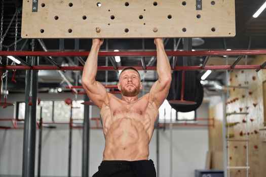 Man climbing pegboard gym athlete training arm strength stamina alpinism indoor. Athlete caucasian guy hanging from his hands wooden campus board warming up to climb Functional Cross training workout