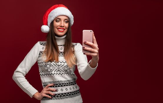 Close up portrait beautifiul caucasian woman in red Santa hat on red studio background. Christmas New Year holiday concept. Cute girl teeth smiling positive emotions with free copy space