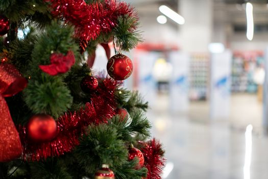 Close Christmas tree in a shopping center against the background of blurry shop windows. Free space for text