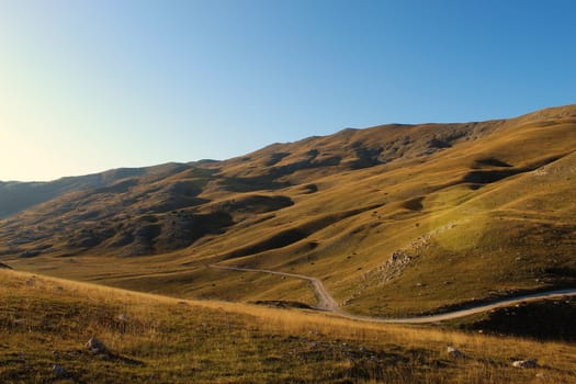 Road through the unevenness of the Bosnian mountain Bjelasnica. The grass in autumn gives a yellow or golden color before sunset. Bjelasnica Mountain, Bosnia and Herzegovina.